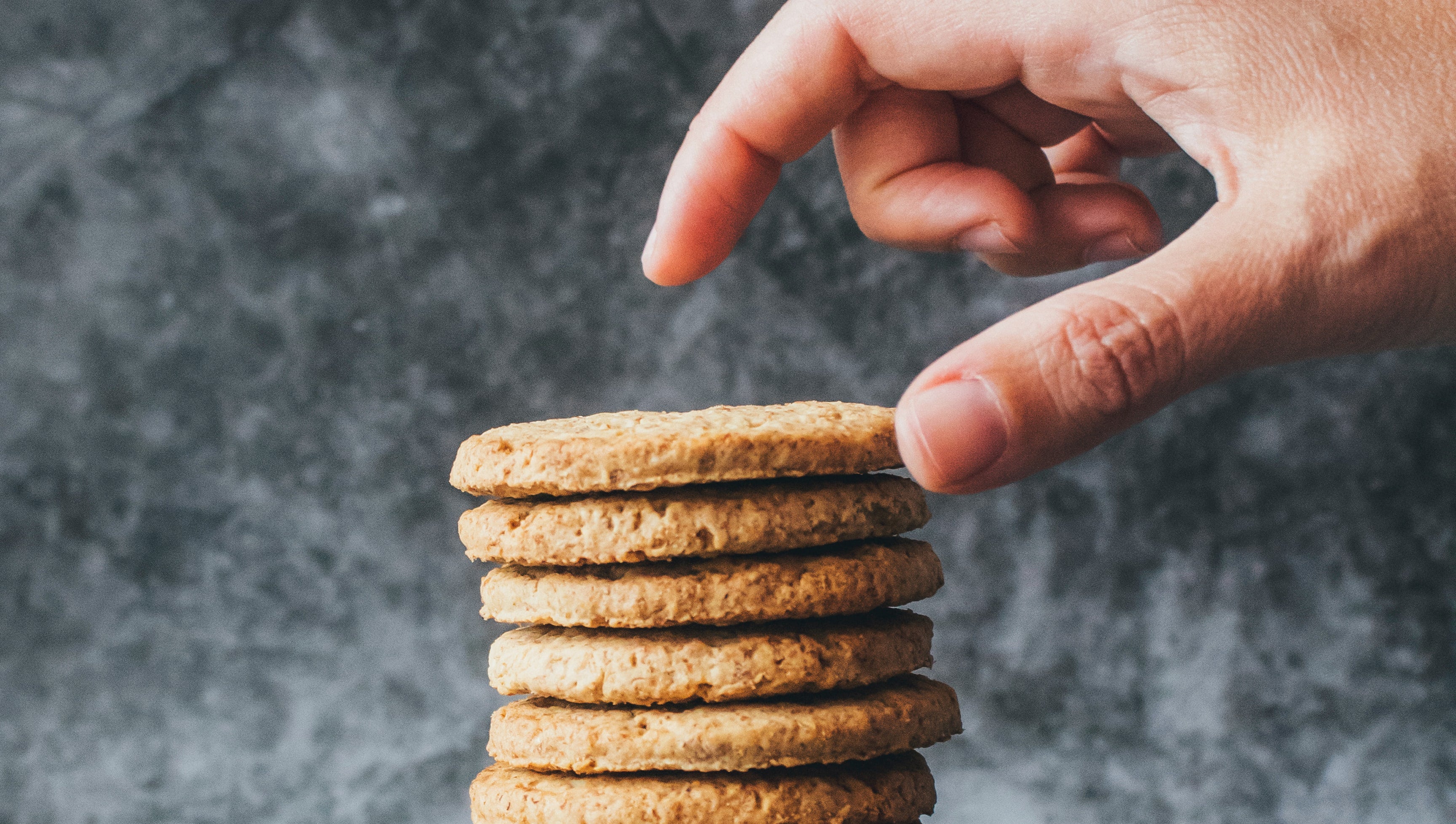 Eine Hand sammelt Kekse von einem Stapel, als bildliche Darstellung einer Website mit Cookie Hinweis, die Cookies der Nutzer:innen sammelt.