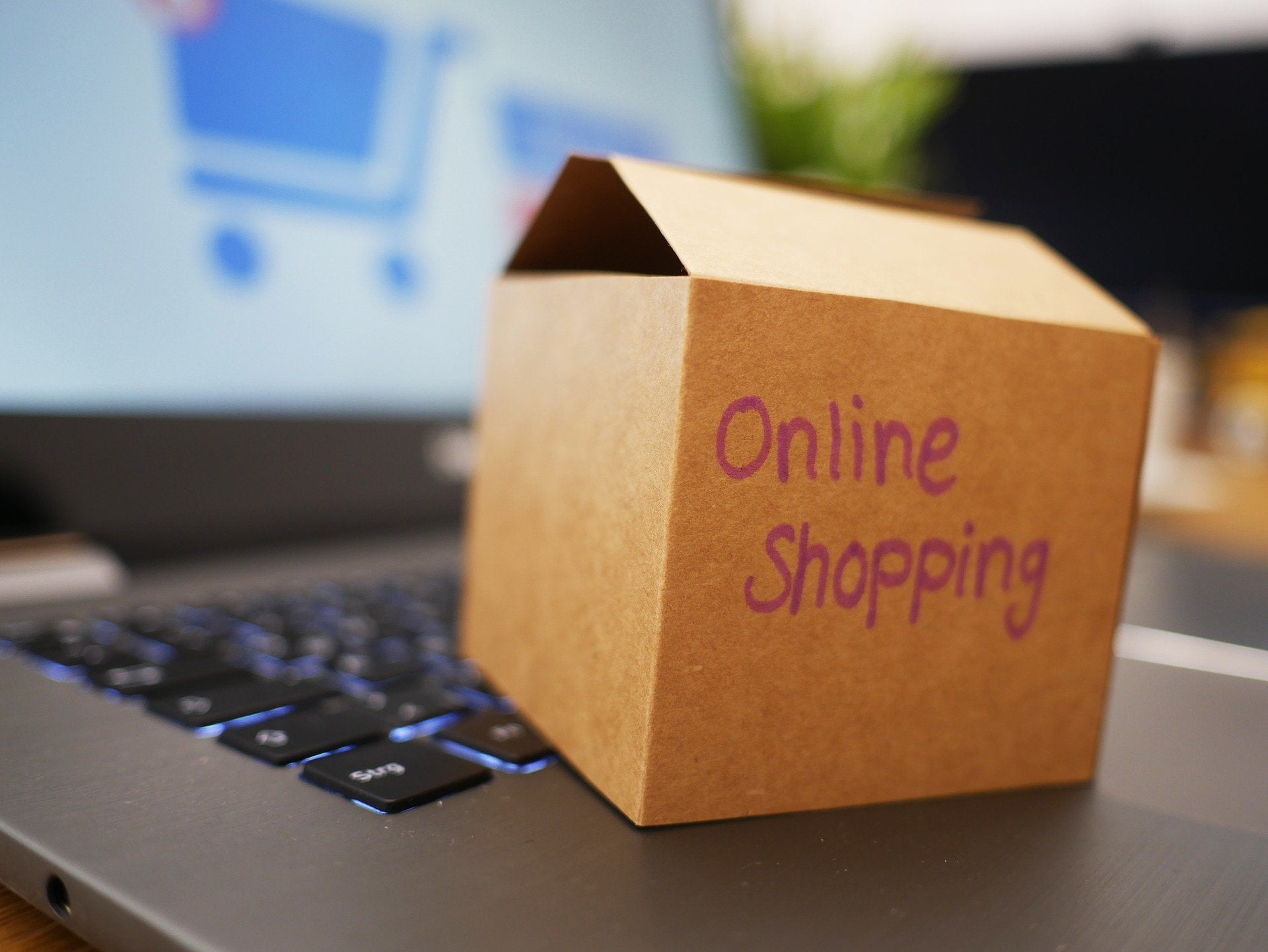 Ein Mini-Paket mit der Aufschrift "Online Shopping" steht auf der Tastatur eines aufgeklappten Laptops. Mit Paketbeilagen sagst du effektiv Danke an deine Kund:innen.