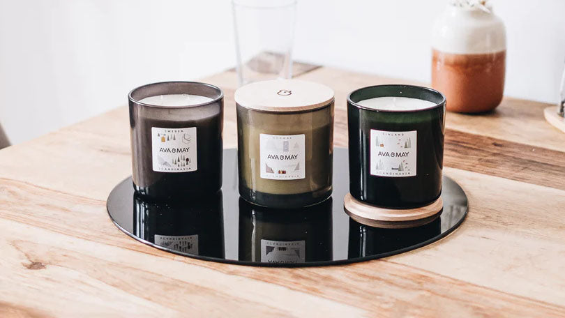 Drei unterschiedliche Kerzen stehen auf einem schwarzen Unterteller auf einem Tisch aus Holz vor einer weißen Wand. Dein DIY-Business kannst du mit Kerzen recht einfach starten. Mehr DIY-Ideen findest du in diesem Beitrag!