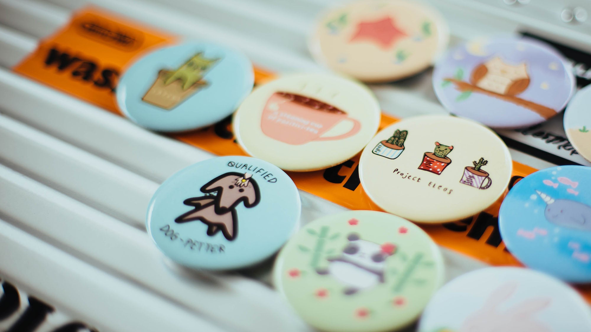 Diverse runde Pins mit unterschiedlichen Motiven und Farben liegen nebeneinander. Emaille Anstecker und Pins können den Einstieg in dein DIY-Business darstellen. Mehr Inspiration findest du in diesem Beitrag!