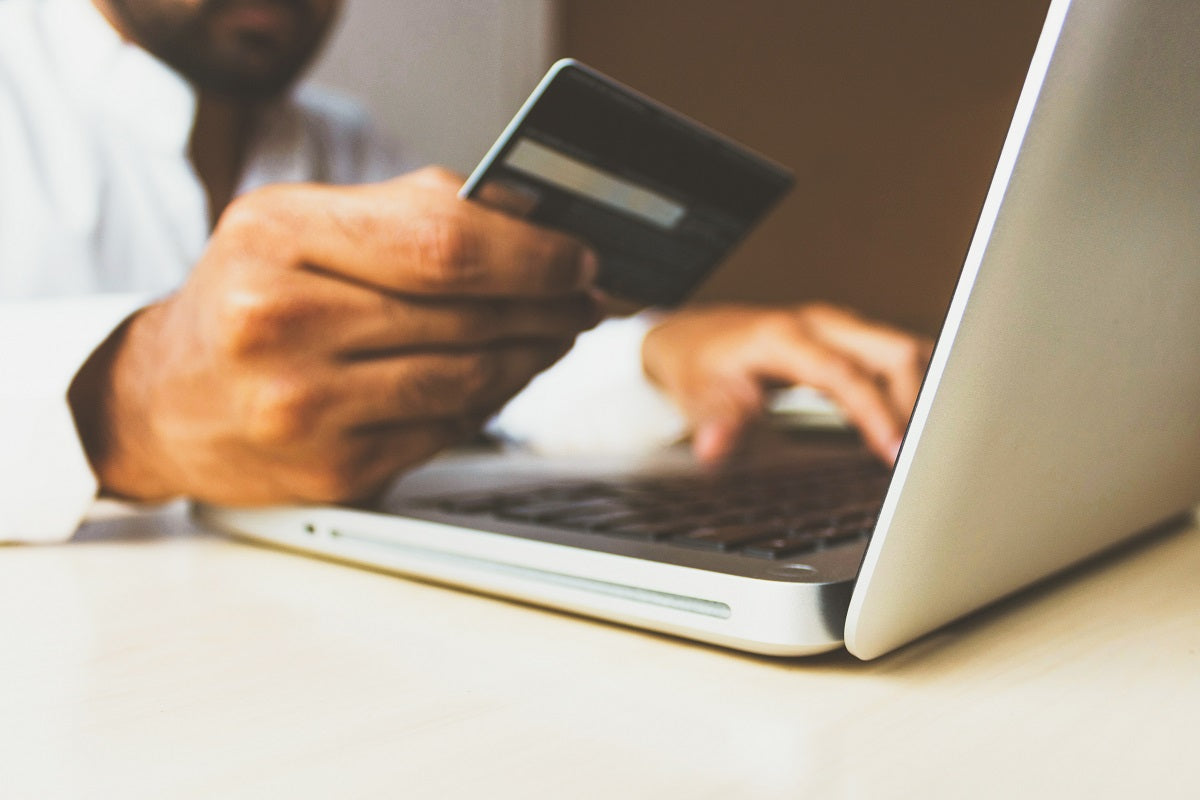 Das Foto zeigt einen Mann, der vor seinem Laptop sitzt und eine Kreditkarte in der Hand hält. Wir zeigen dir, mit welchen Domain Kosten du rechnen musst.