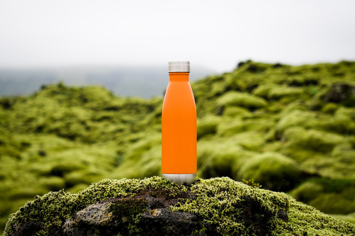 Das Foto zeigt eine orangene Trinkflasche, die auf einer grünen Landschaft steht.