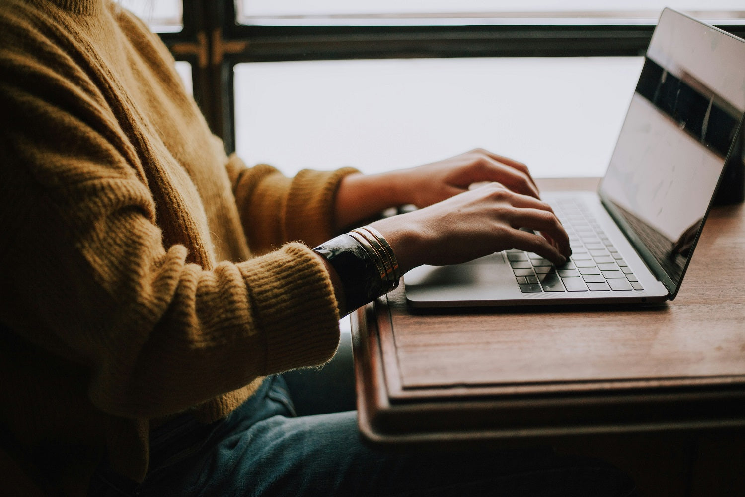 Das Foto zeigt eine Frau, die an einem Schreibtisch sitzt und an ihrem Laptop arbeitet
