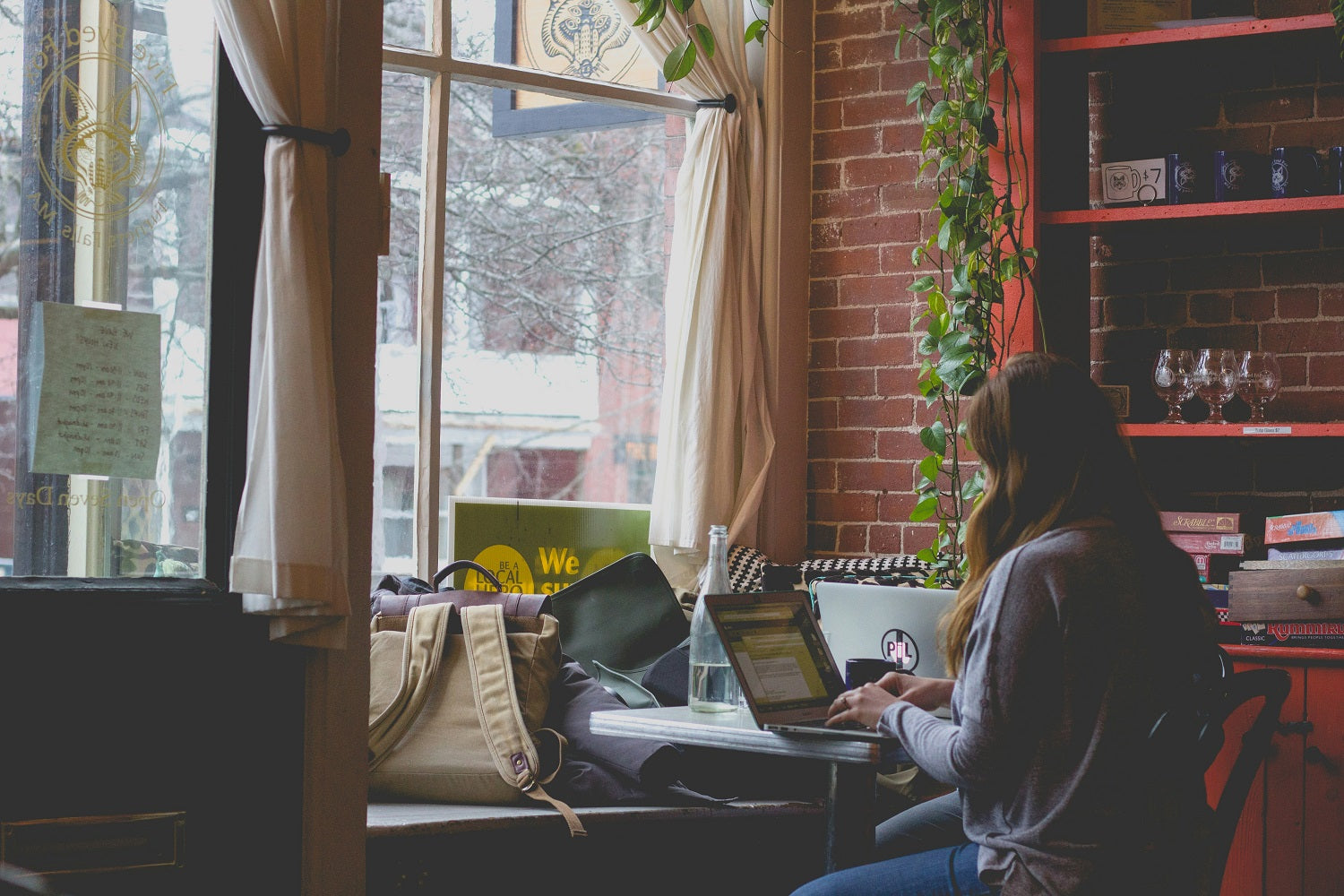 Das Foto zeigt eine Frau, die in einem Café sitzt und an einem Laptop arbeitet.