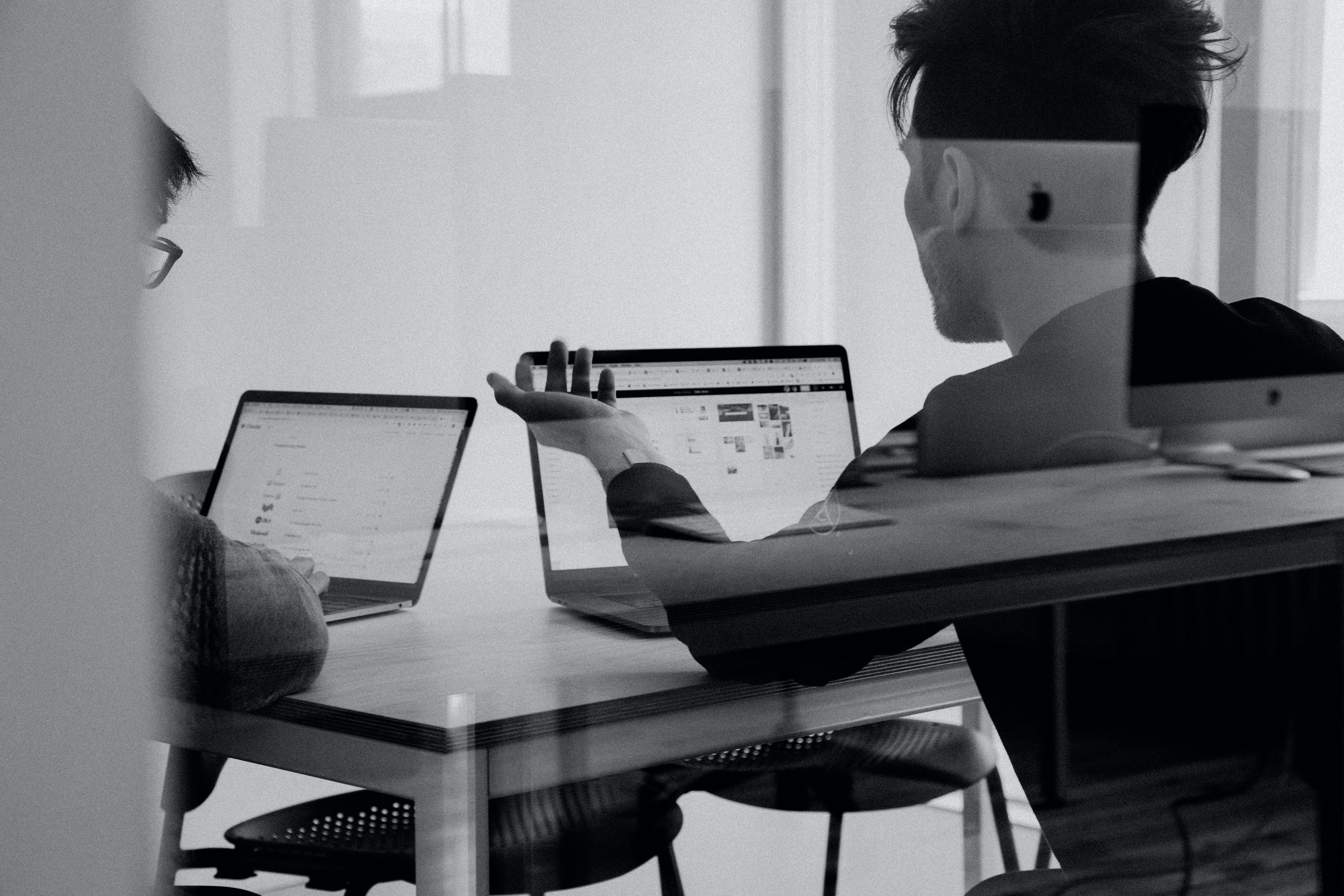 Ein schwarz-weiß Bild bei dem man zwei Menschen in einer Spiegelung sieht, die am Laptop sitzen und über eine Executive Summary reden