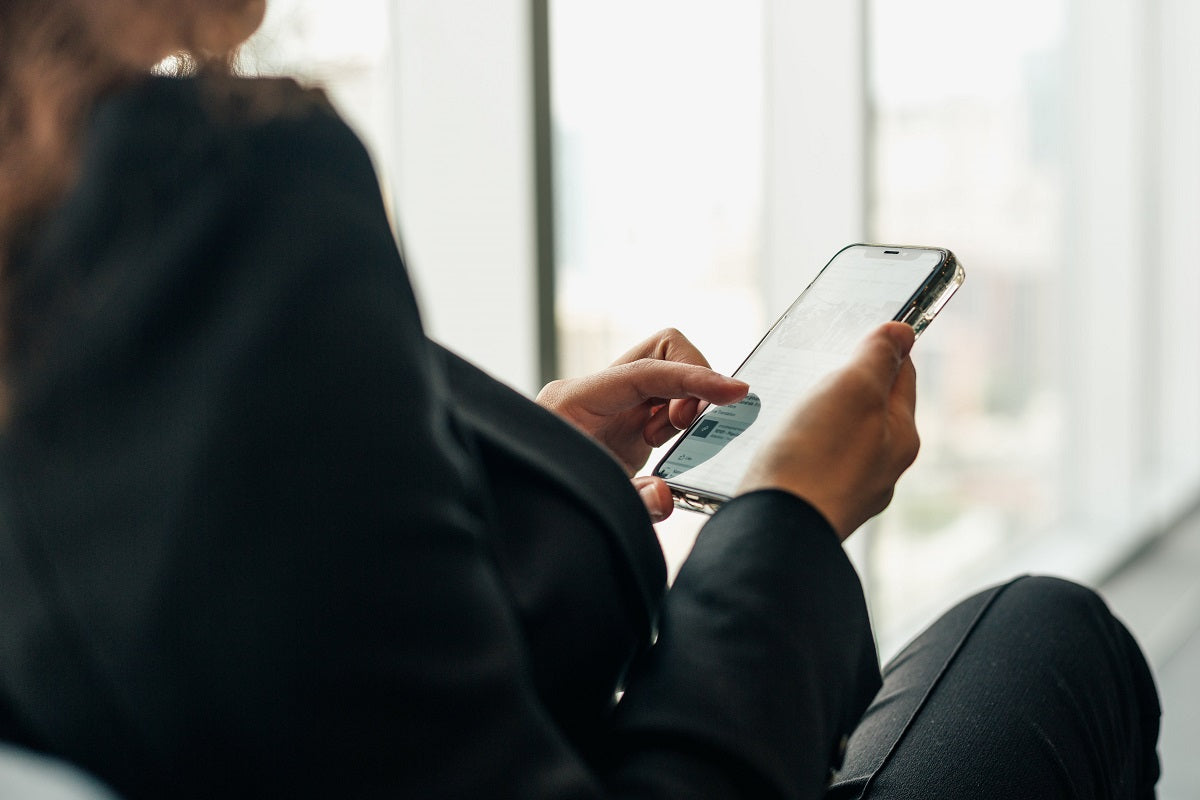 Eine Frau sitzt rückwärtsgewandt mit einem Handy in den Händen vor einer Glasfront. Du willst dein Handy gar nicht mehr aus der Hand legen, wenn du deine Facebook Ads mit unseren Tipps auf ein neues Level hebst!