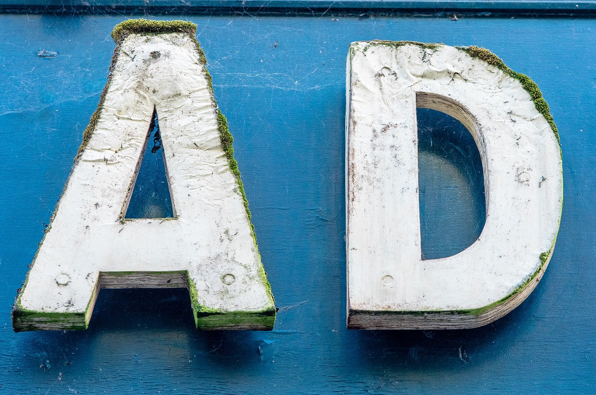 Zwei weiße, bereits mit Moos bewachsene Buchstaben einer alten Anzeigetafel formen vor blauem Hintergrund das Wort „AD“. Damit deine Werbekampagne kein Moos ansetzt, zeigen wir dir, wie du deine Facebook Ads richtig skalierst!