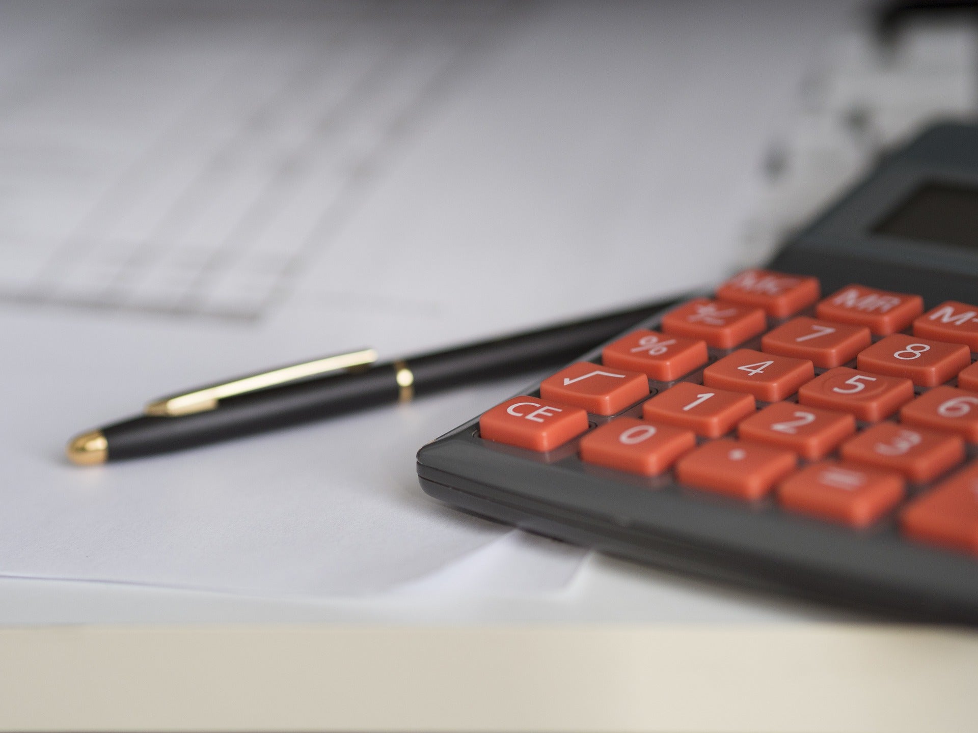 Auf einem Tisch liegen Dokumente sowie ein Taschenrechner mit roten Tasten und ein Kugelschreiber. Nachdem du dein Gewerbe angemeldet hast, folgt ein Fragebogen vom Finanzamt.