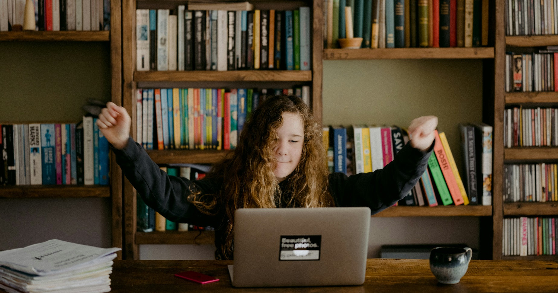 Das Foto zeigt ein junges Mädchen, dass vor einem Laptop sitzt und die Arme in die Luft streckt. Wie das Gewerbe anmelden unter 18 gelingt, zeigen wir dir im Blogbeitrag.