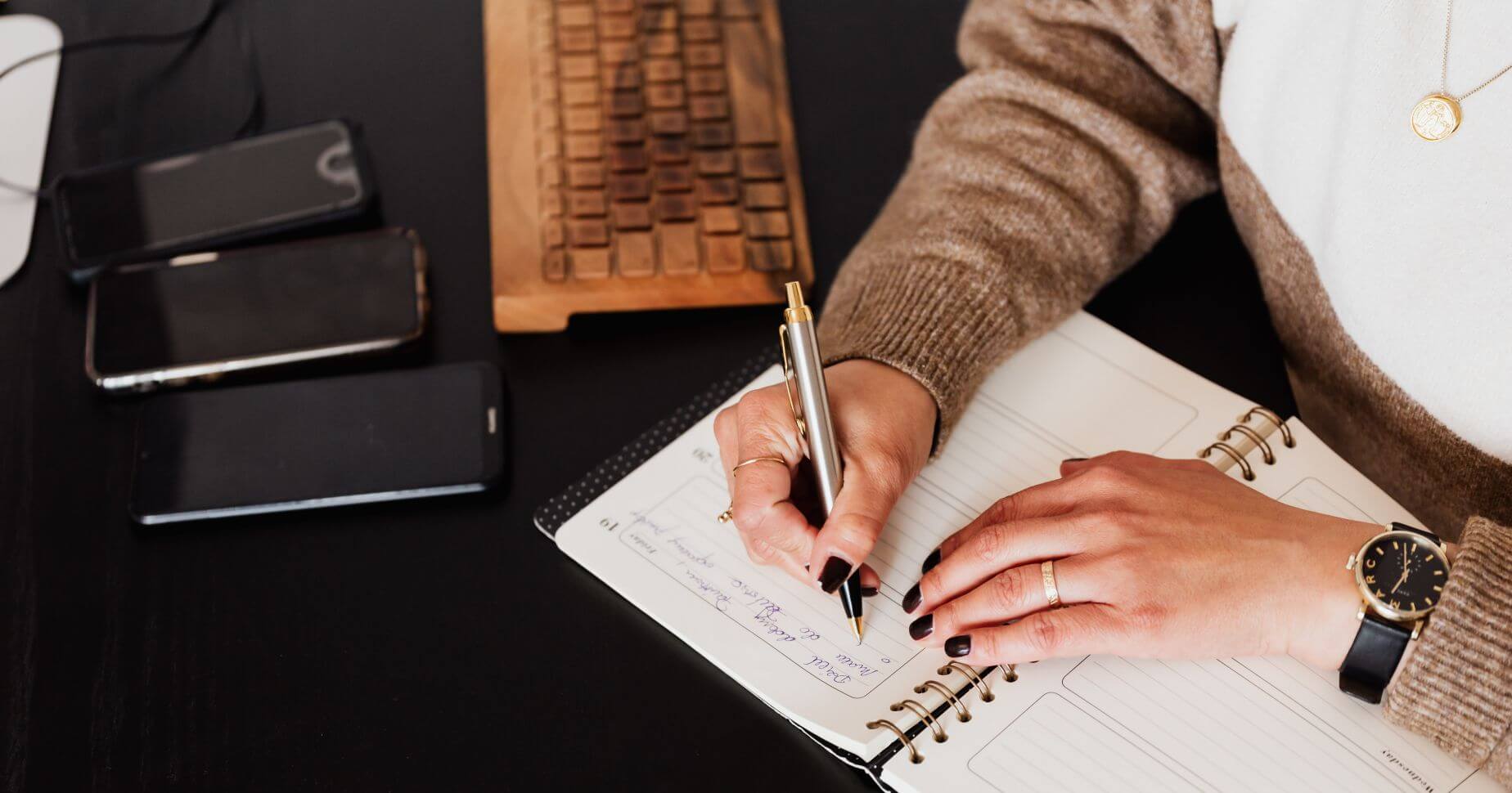 Eine Frau im Pullover am Schreibtisch, die in ihr Notizbuch schreibt, um eine GmbH zu gründen
