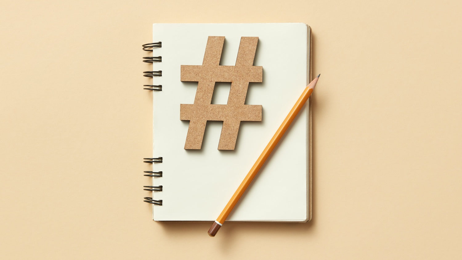 Notizblock auf dem ein Bleistift und ein Hashtag aus Papier liegt