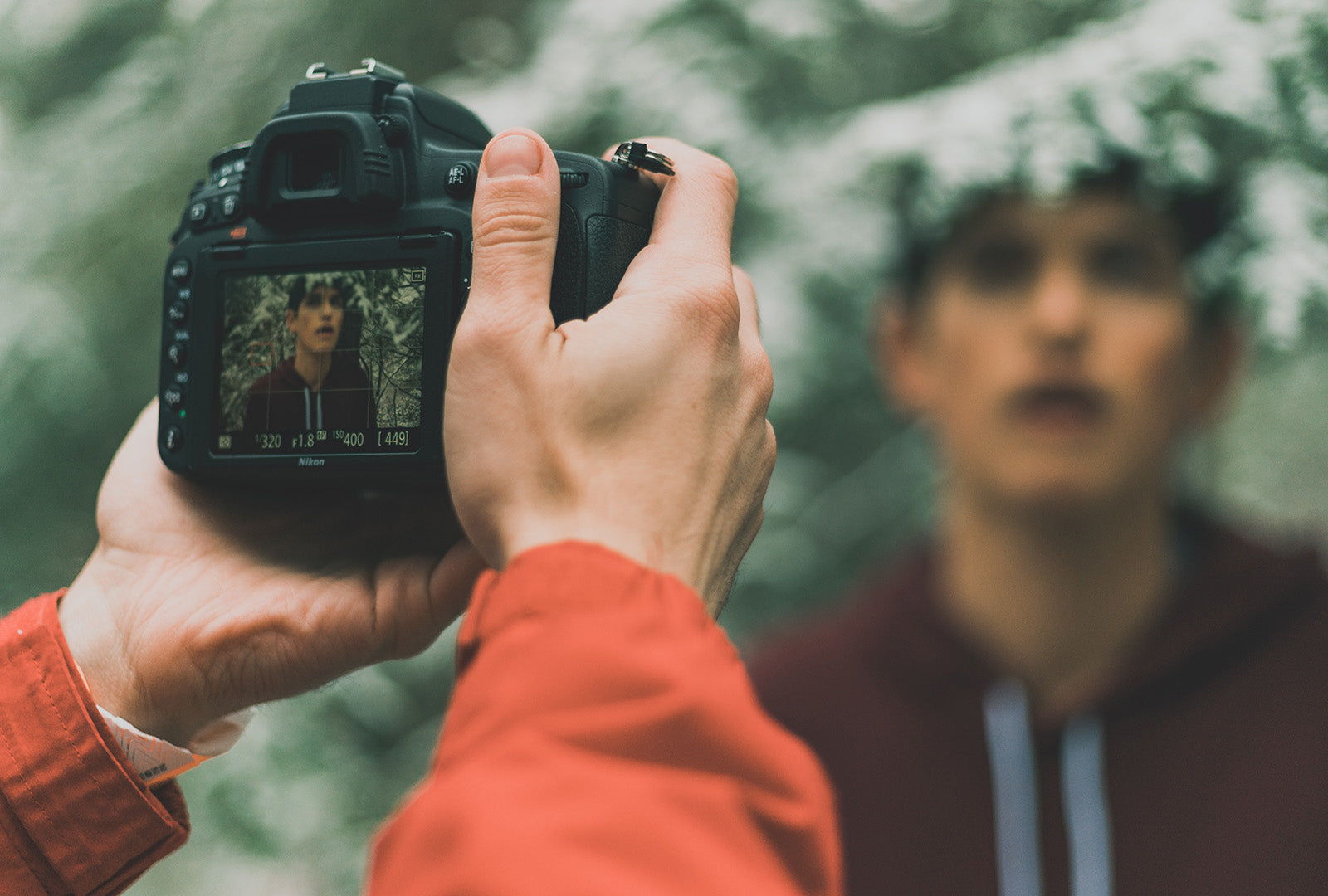 Zwei Hände halten eine Kamera und fotografieren Kleidung an einem Model in einem Wald.