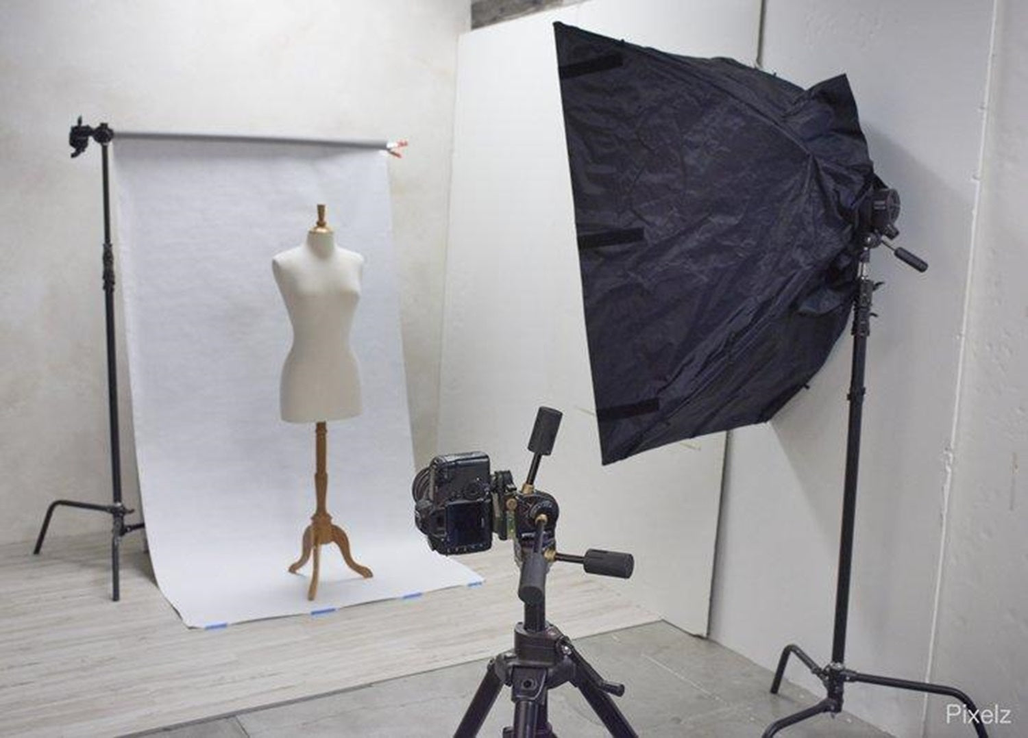 In einem Fotostudio steht eine Kamera, eine Schneiderpuppe, Beleuchtung und Hintergründe bereit, um Kleidung zu fotografieren