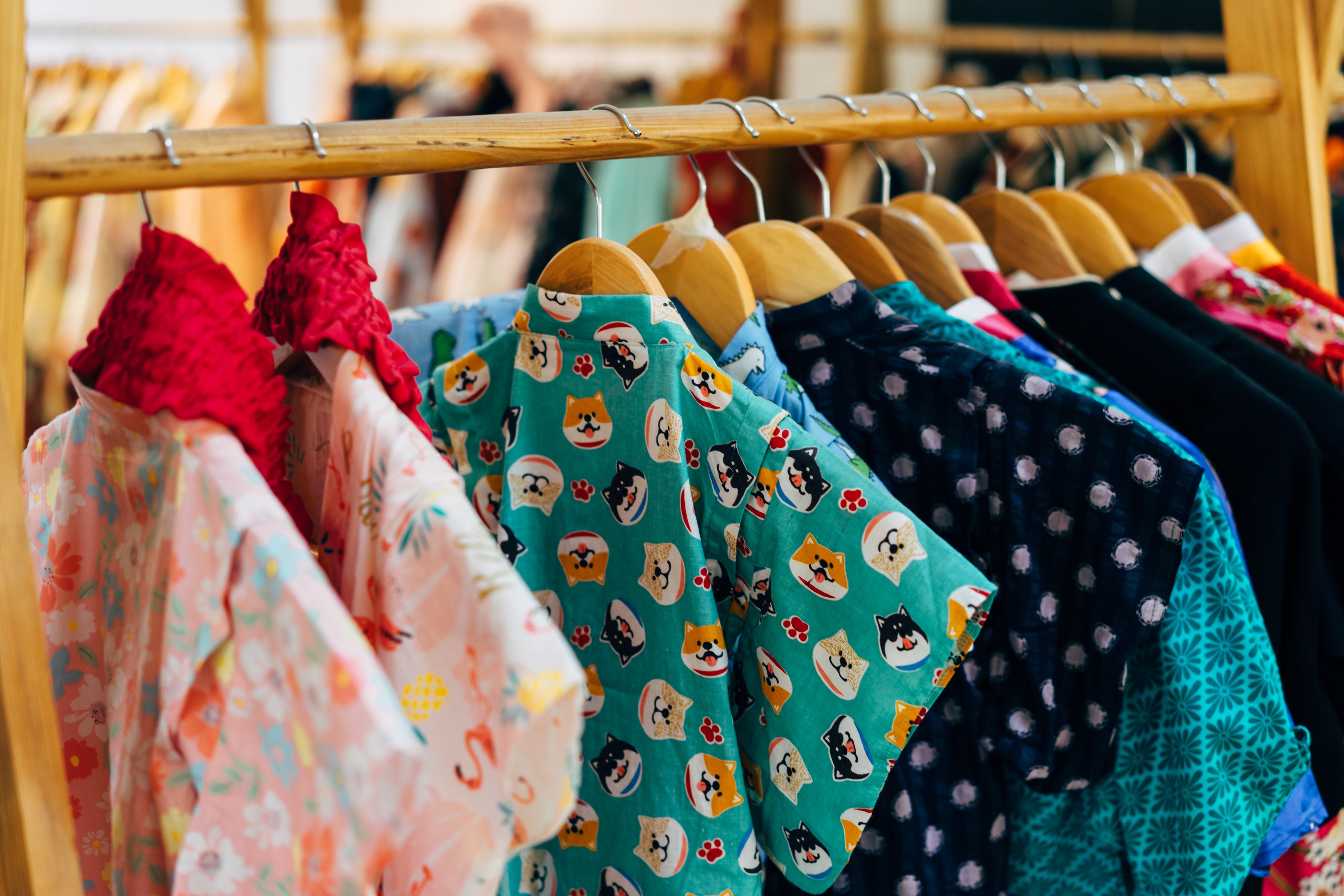 Auf einer Kleiderstange aus Holz hängen diverse T-Shirts in Kindergrößen. Die deutsche Textilindustrie hat eine lange Tradition. Trotz Billigproduktion im Ausland wahren einige Anbieter:innen die heimische Produktion. Wir zeigen dir, welche Anbieter:innen Kleidung in Deutschland produzieren lassen.