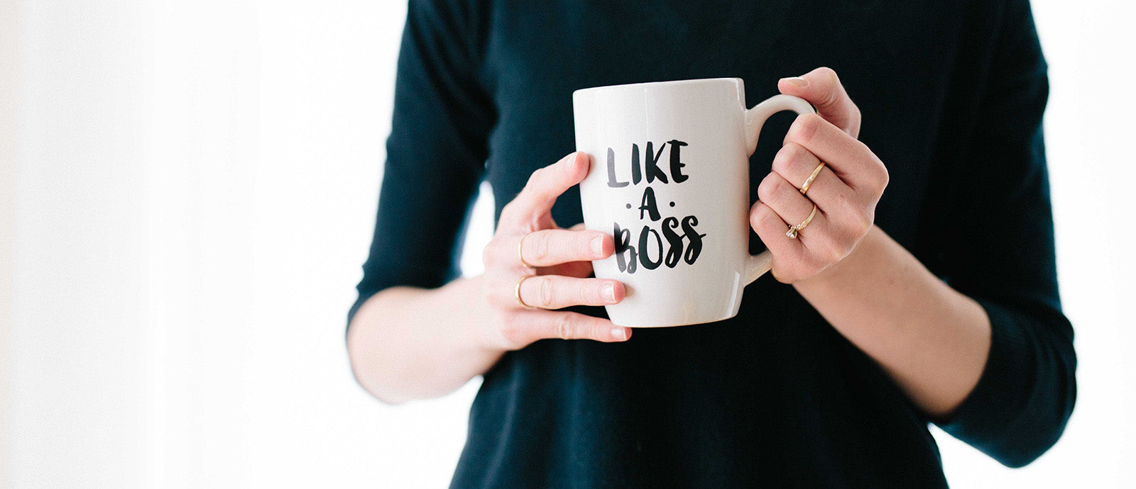 Eine Person, die die Kleinunternehmerregelung in Anspruch nimmt, hält eine Tasse mit der Aufschrift "Like A Boss" in den Händen