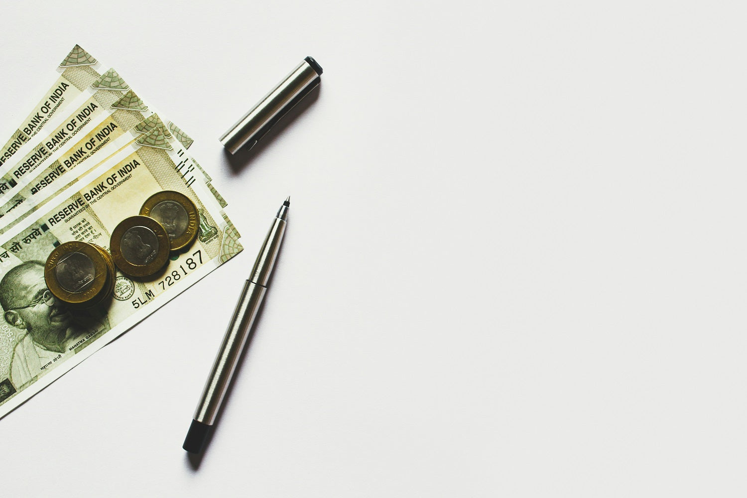 Auf einem weißen Hintergrund liegen Geldscheine, Geldmünzen und ein offener Kugelschreiber.