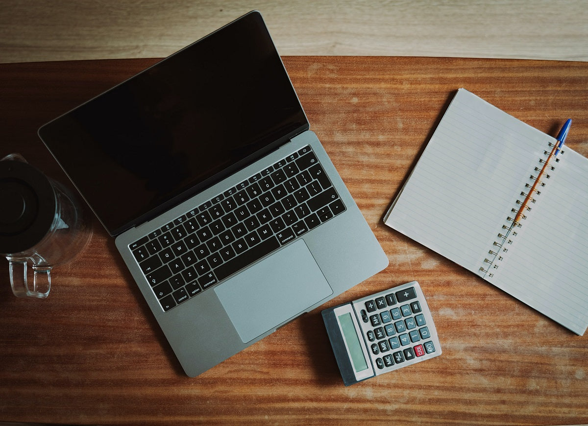 Auf einem Schreibtisch liegt ein Laptop, ein Taschenrechner und ein Notizbuch. Wir zeigen dir, wie du Schritt für Schritt eine Lohnabrechnung erstellen kannst.