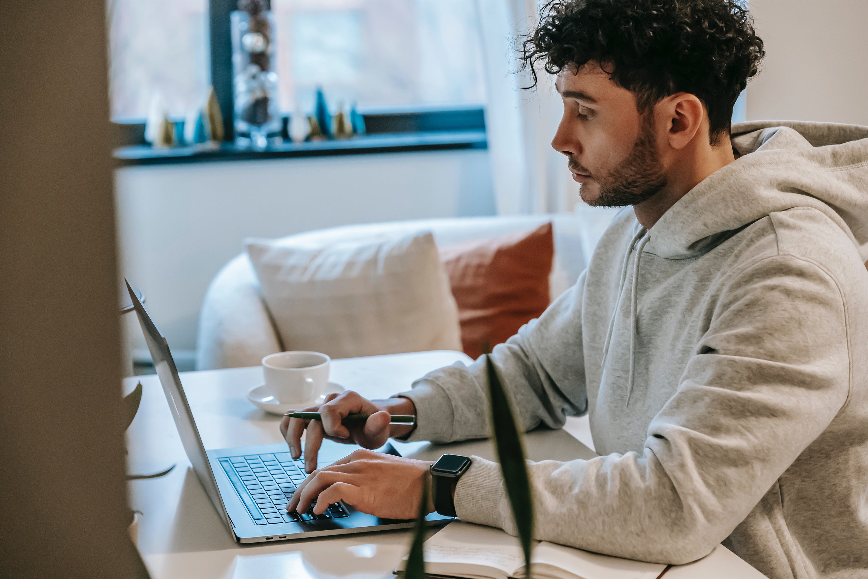 Ein Mann im hellen Hoodie, der am Schreibtisch sitzt und an seinem Laptop ein Nebengewerbe anmelden will