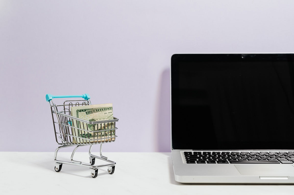 Das Foto zeigt einen Einkaufswagen und einen Laptop. Beim Verkauf von Waren kommen mit der Omnibusrichtlinie neue Verordnungen auf Händler:innen zu.