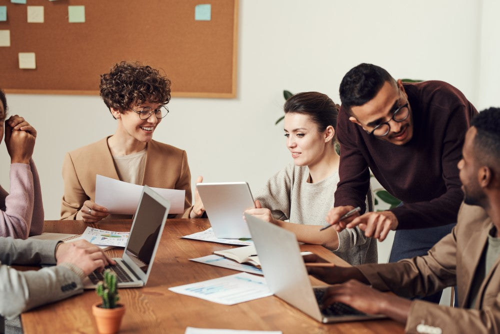 Personen an Schreibtisch mit Formularen und Laptops