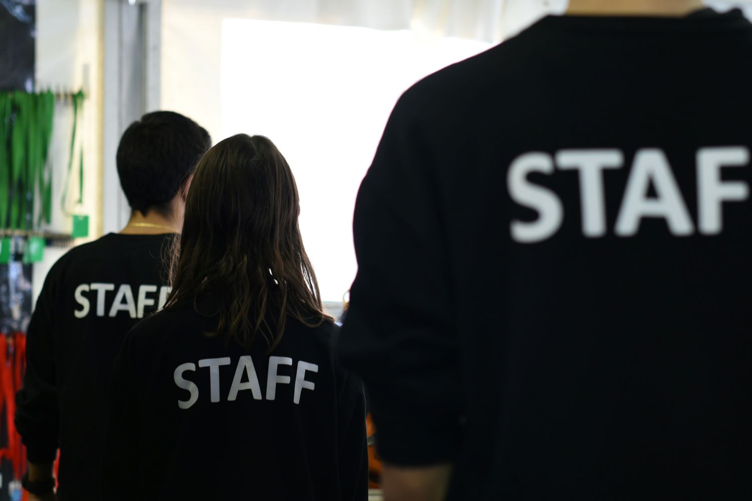 Das Bild zeigt einige Personen mit schwarzen T-Shirts von hinten. Auf den T-Shirts steht "Staff".