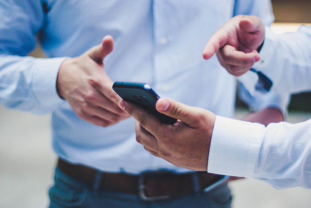 Zwei Männer halten ein Smartphone in der Hand und diskutieren. Die wichtigsten Aspekte für deine Entscheidung für eine POS-App stellen wir dir im Beitrag vor.