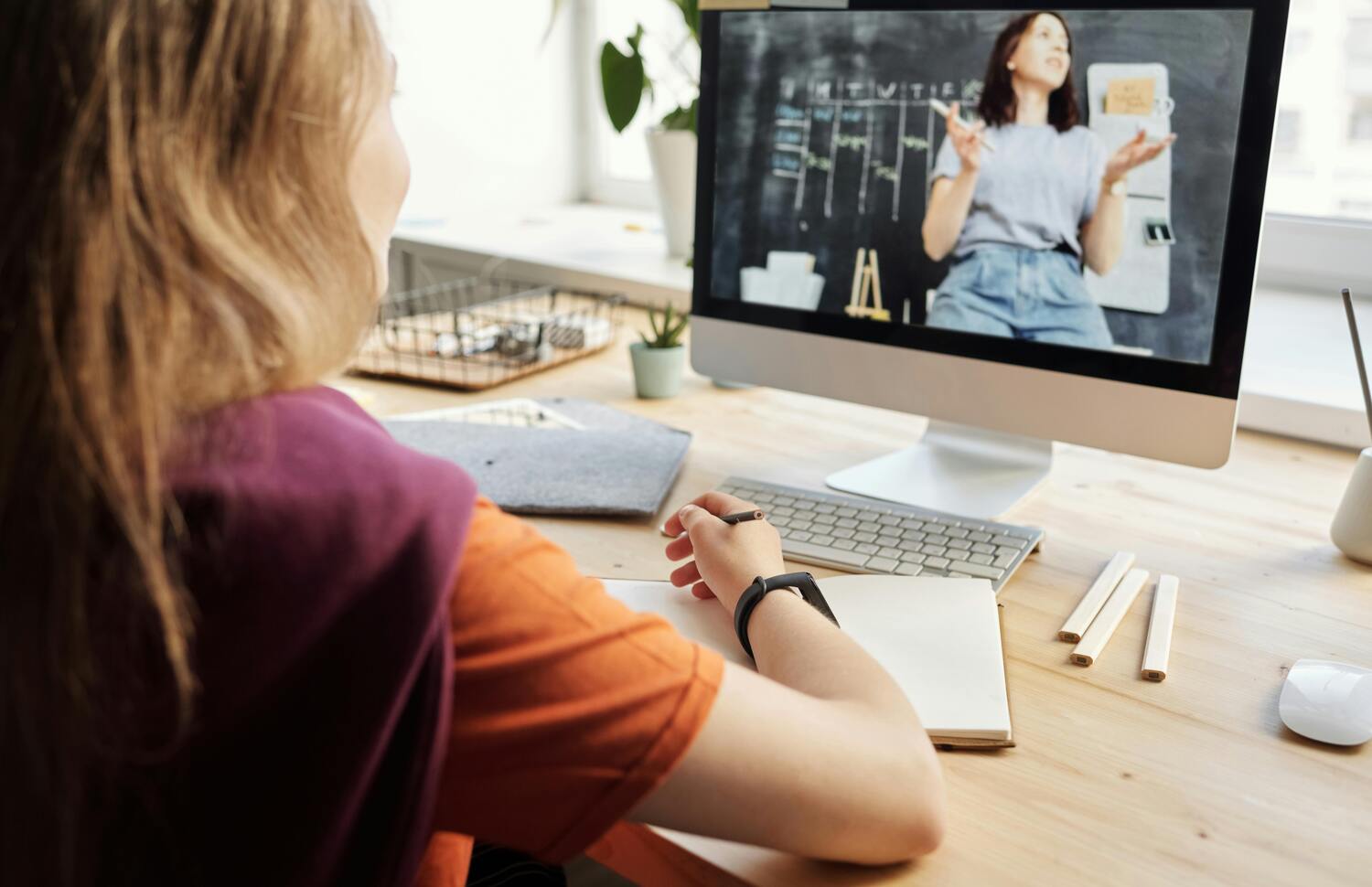 Frau mit Notizblock vor Computerbildschirm mit Webinar