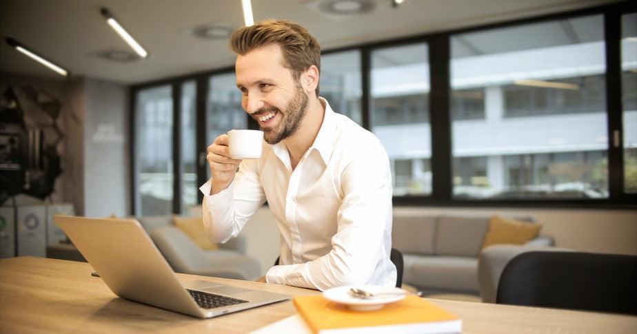 Bild eines Mannes grinsend vor seinem Laptop als visuelles Beispiel von einem Shop Manager