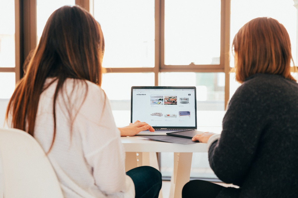 Zwei Frauen sitzen vor einem Laptop und sehen sich eine Website an. Wir stellen dir die Vorteile von Shopify vs. Shopify Plus vor.