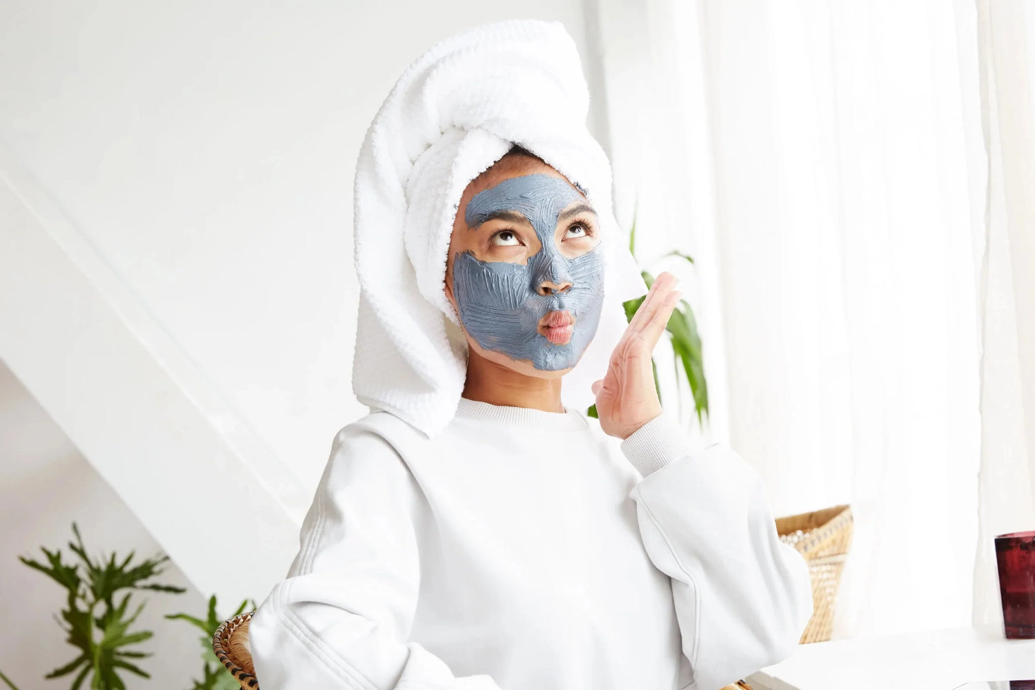 Person mit einem Handtuch auf dem Kopf und einer Tonmaske posiert mit einem lustigen Gesichtsausdruck