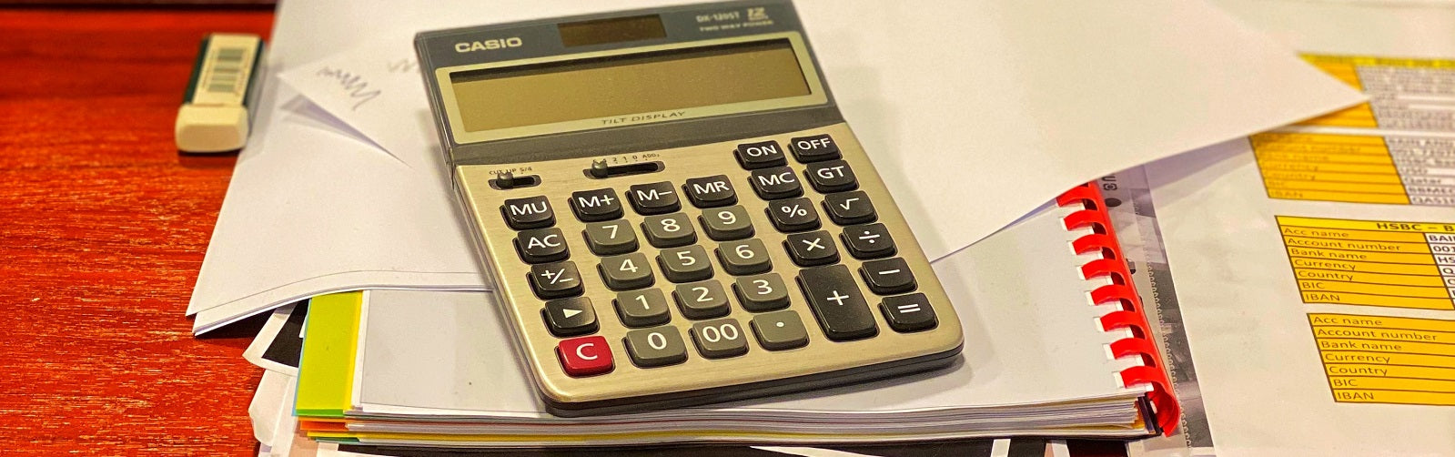 Ein Taschenrechner liegt auf einem Stapel Papier auf einem Schreibtisch, um die Umsatzsteuervoranmeldung anzugehen.