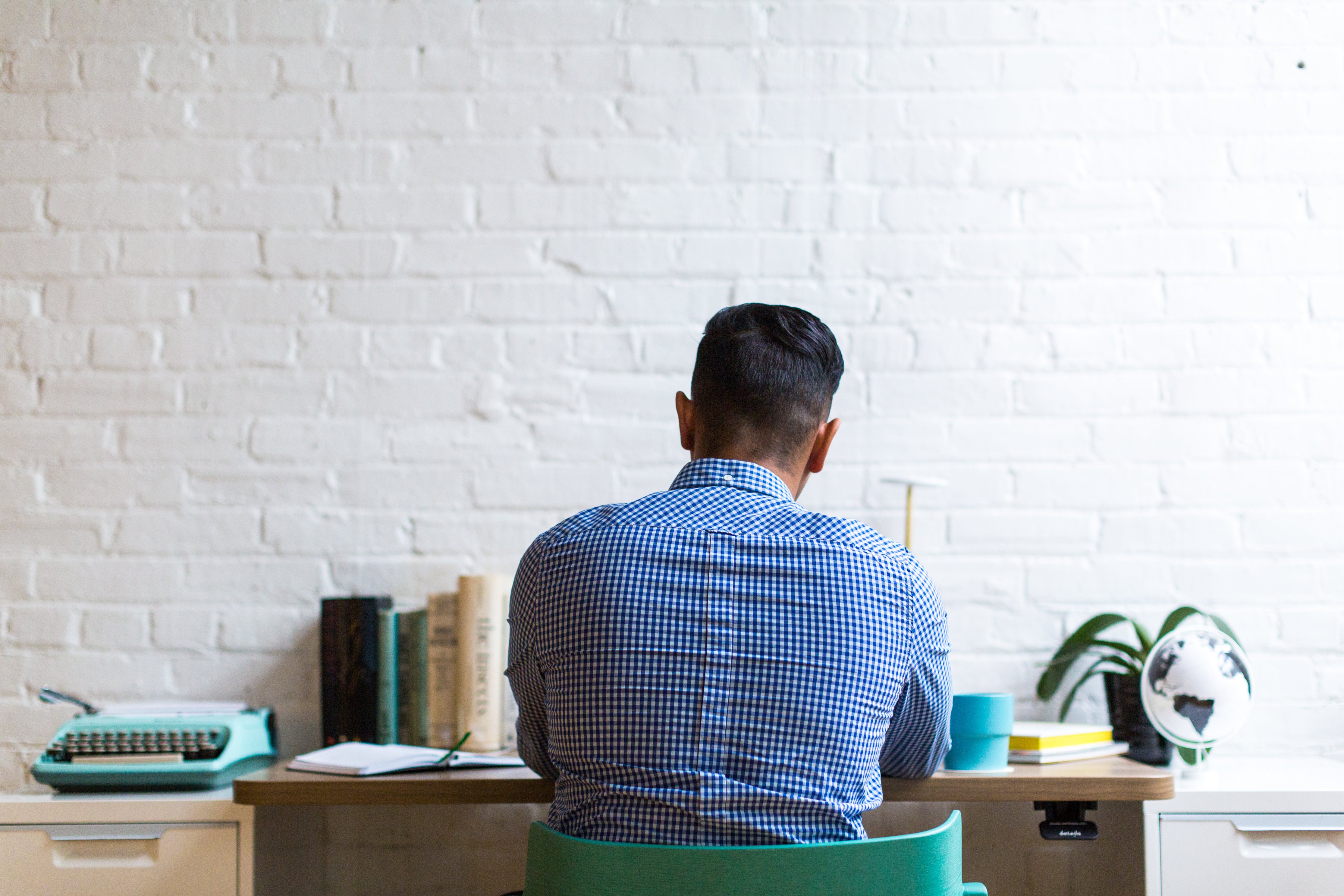 Ein junger Mann im blauen Hemd sitzt mit dem Rücken zugewandt an einem Schreibtisch vor einer weißen Wand und arbeitet. Neben einer guten Idee ist beim Gründen einer Firma auch ein gewisser Schutz des Unternehmens nötig. Wir zeigen dir, welche Versicherungen du benötigst!