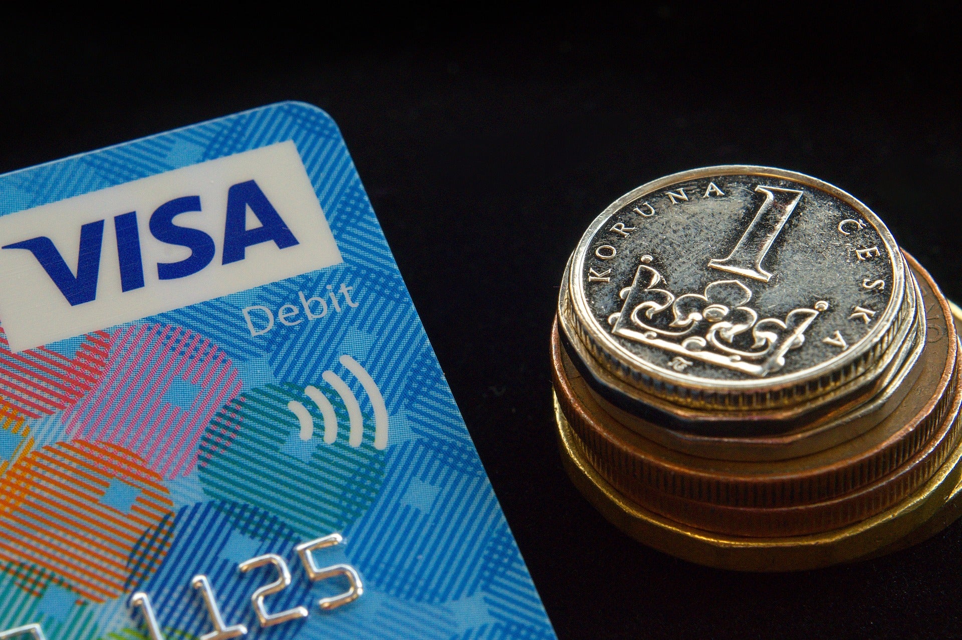 Ein Stück einer Kreditkarte mit dem VISA-Schriftzug ist neben einem Stapel ausländischer Münzen vor schwarzem Hintergrund zu sehen. Gestalte deine Preise individuell je nach Wechselkurs, um weltweit zu verkaufen.