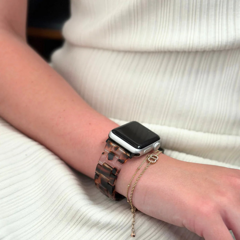 Person wearing a smartwatch with a tortoiseshell band and a delicate gold bracelet.