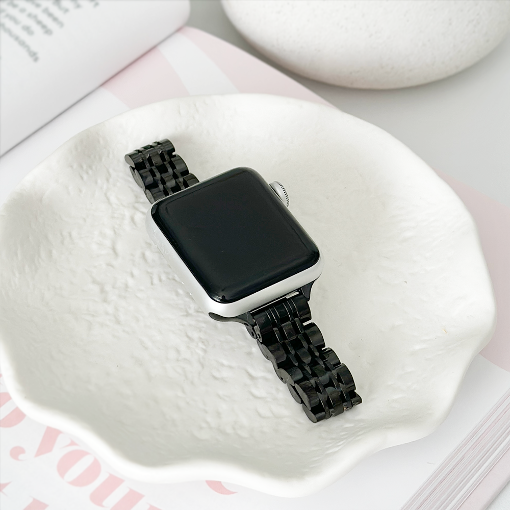 A smartwatch with a black metal strap resting on a white textured dish.