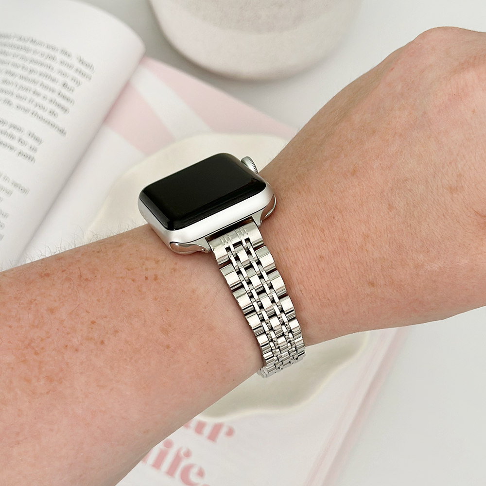 A person wearing a smartwatch with a metal band, reading an open book.