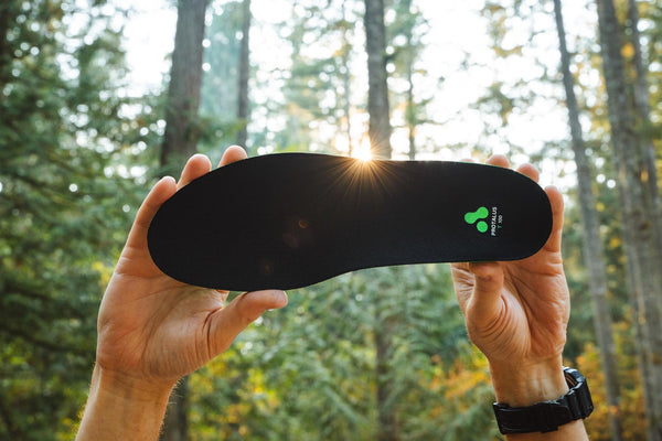 2 hands holding up a T-100 Elite insole in the forest