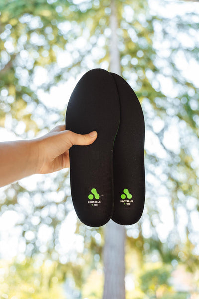 Hand holding out Protalus T-100 Elite Insoles with trees and sunny background