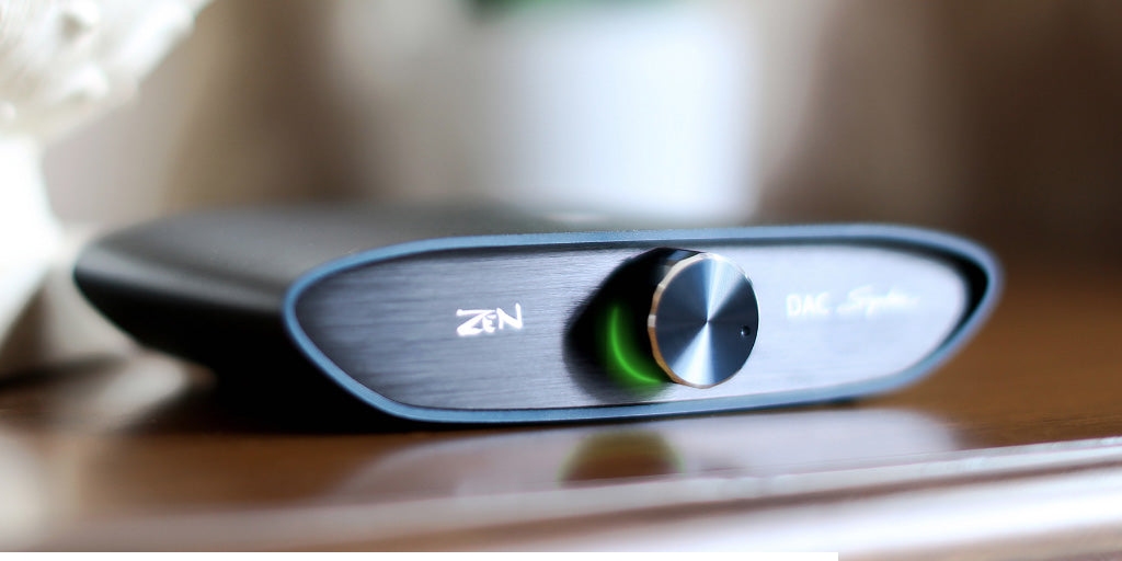 ZEN DAC Signature V2, on desk in home setting with lit dial | Headphones.com