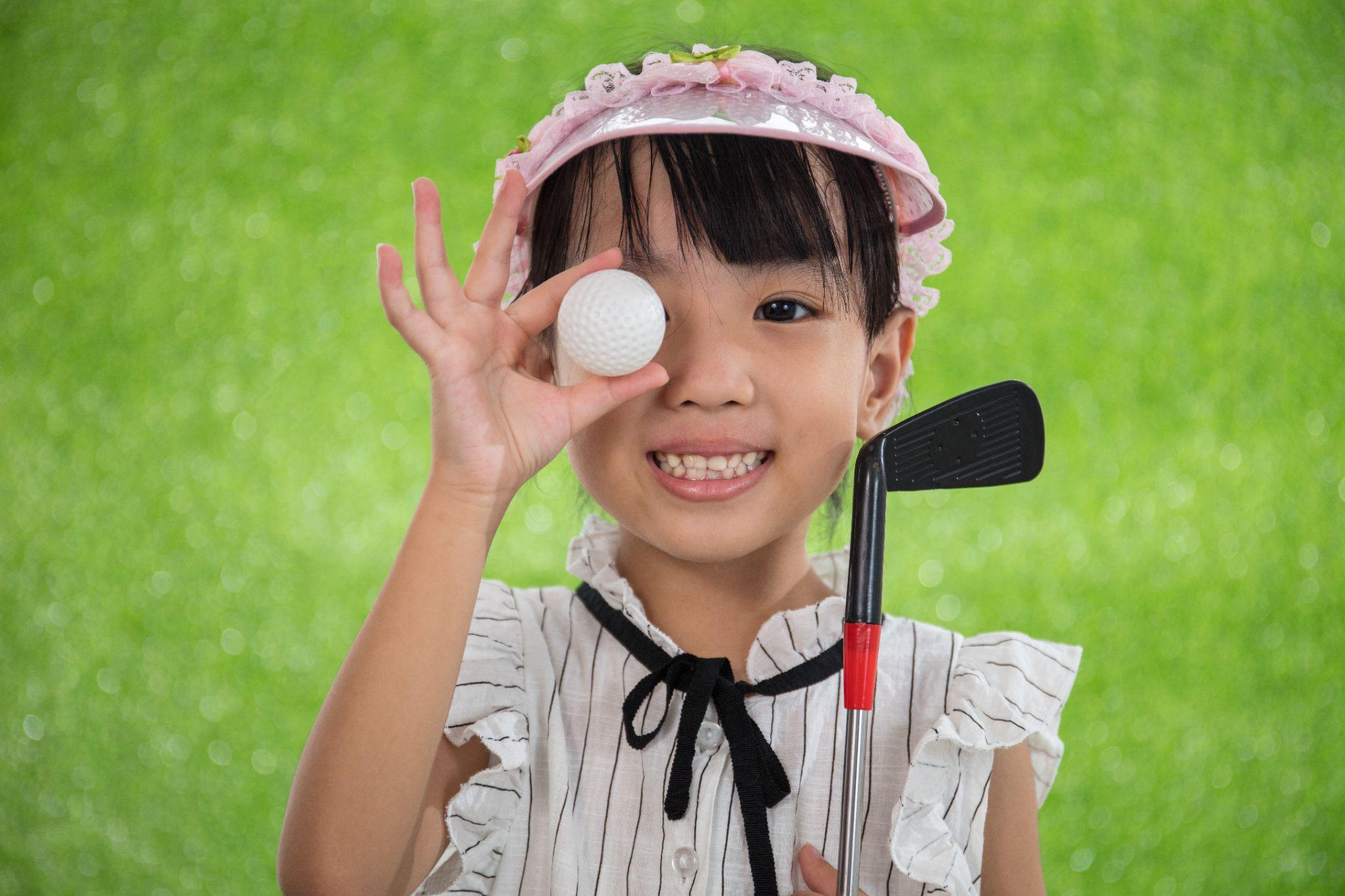 Asian little girl holding a golf ball on green grass