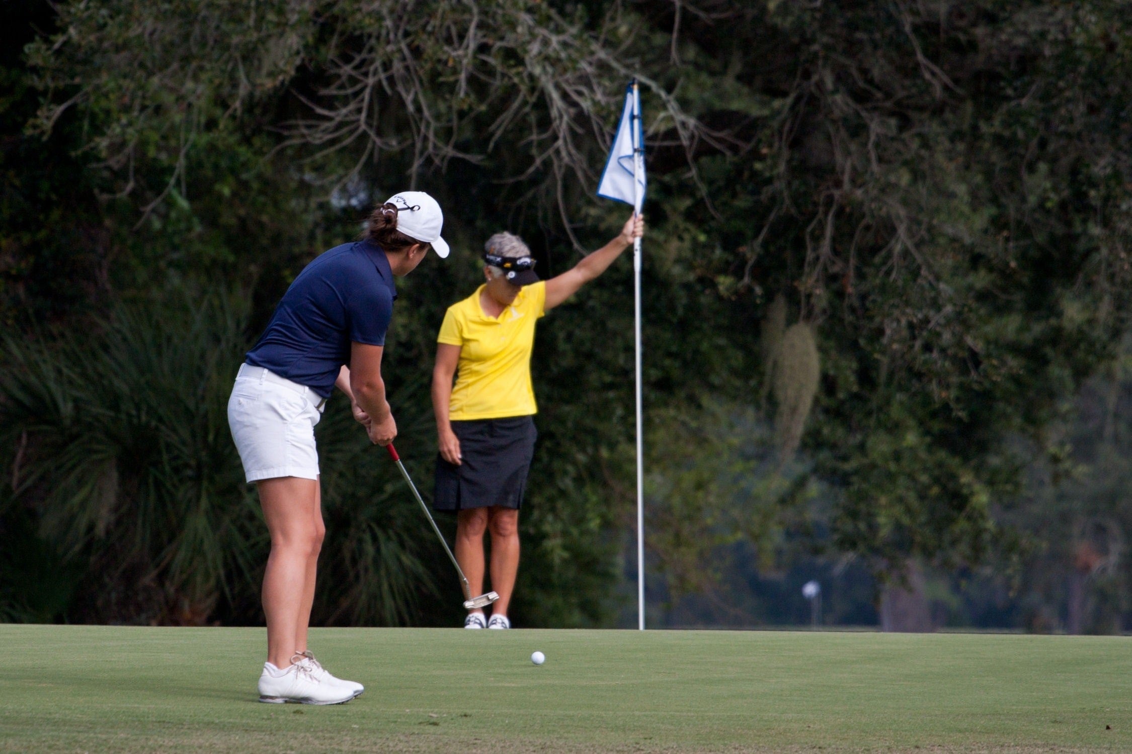 woman putting golf ball while the other woman holds the flag