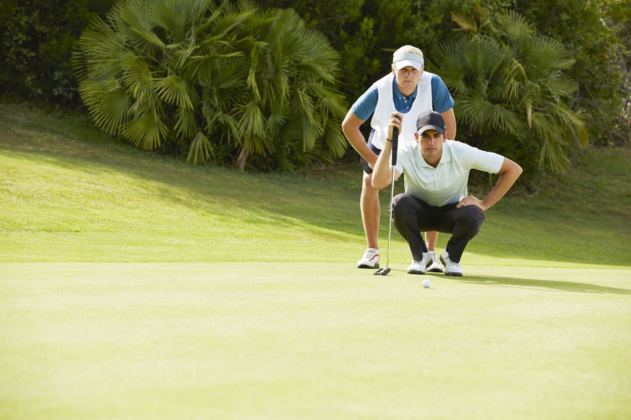Two men anxiously watching a golf ball rolling towards the hole on the green