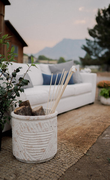 A white basket holds sticks with smores on them. In the background is a white couch with pillows.