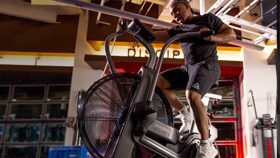 A man is riding an airbike in a gym