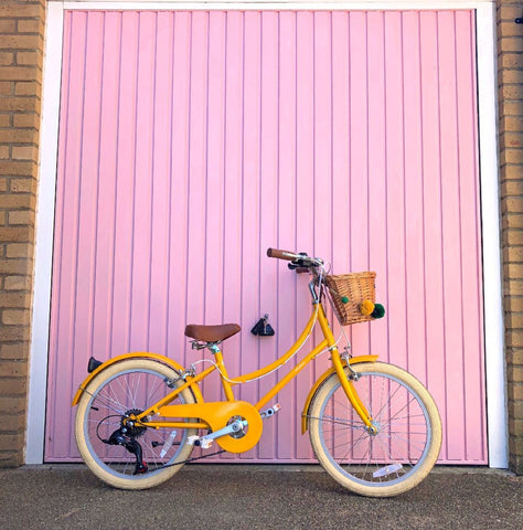 Un vélo Gingersnap Bobbin jaune s'appuya contre une porte de garage rose