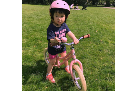 Girl wearing a pink helmet riding a pink balance bike in a grassy park