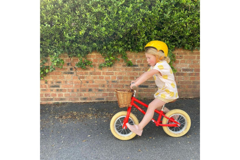 Girl wearing a yellow helmet riding a red balance bike on the pavement