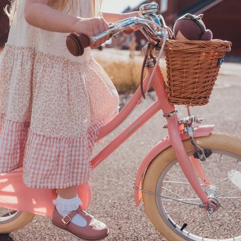 Jeune fille en robe fleurie portant un vélo rose avec un panier