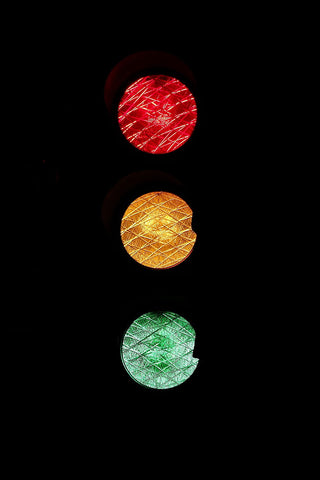 A traffic light showing red, yellow, and green lights, illuminated in the dark.