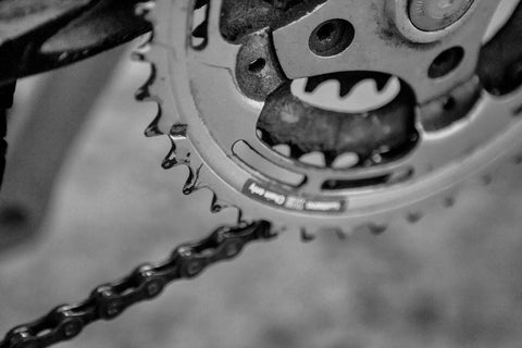 A close-up B&W image showcasing the intricate mechanics of bike gears, highlighting the chain, cassette, and derailleurs.